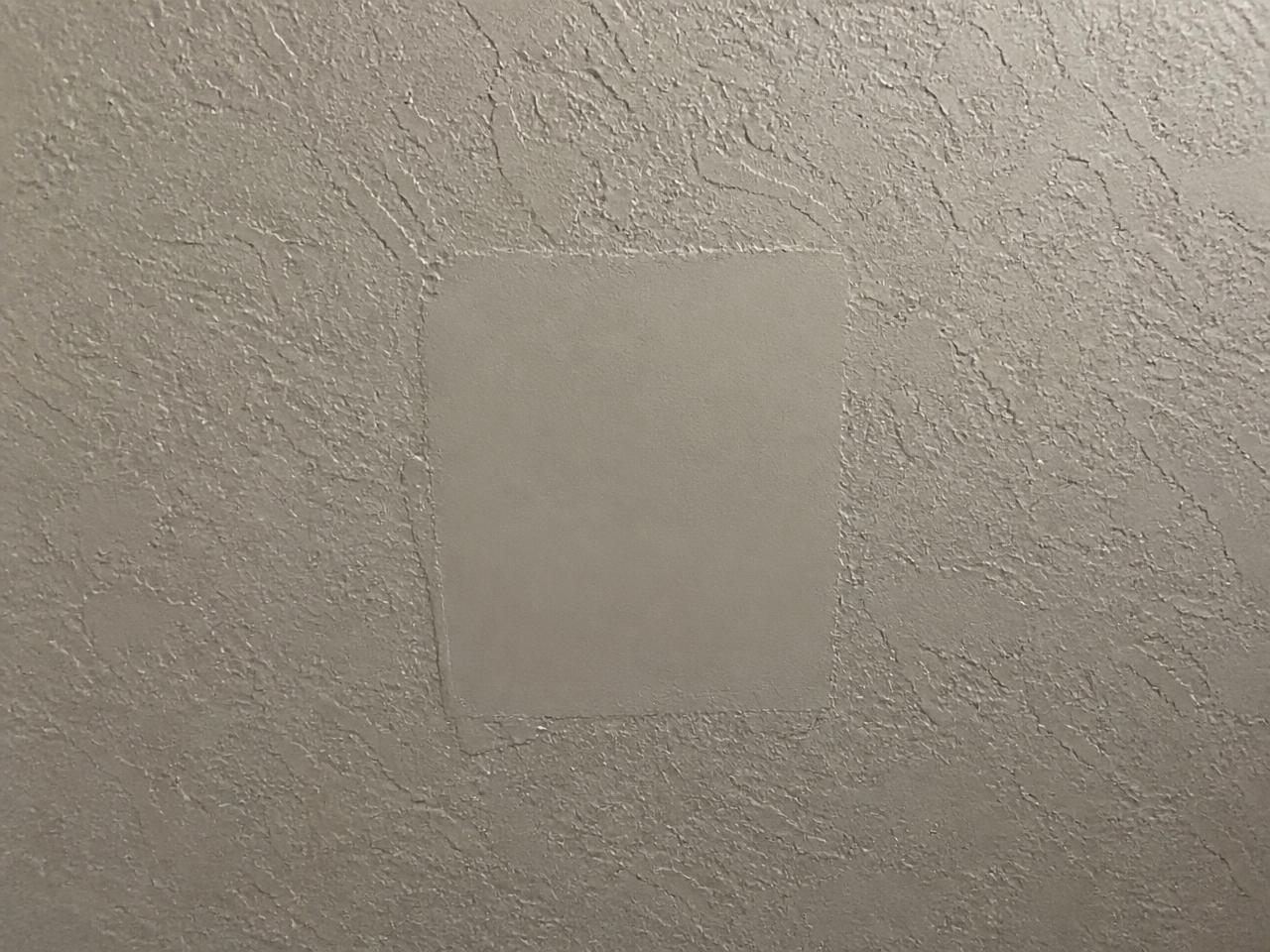 Knockdown-textured wall with a smooth, mismatched patch square visible in raking light.